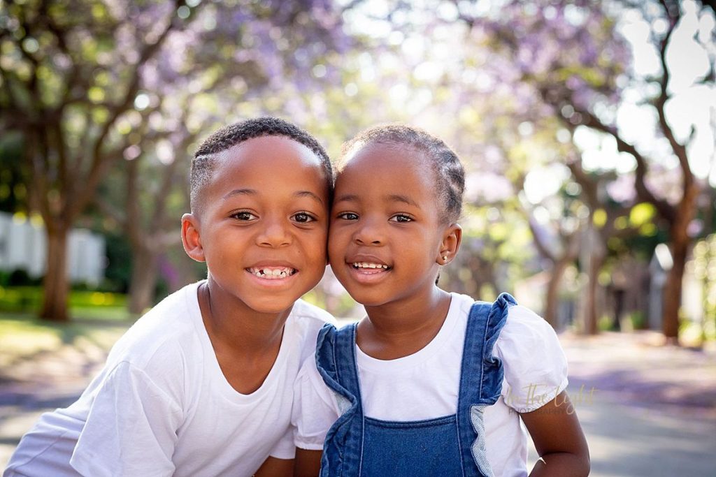Siblings smiling under purple Jacaranda trees in Pretoria.