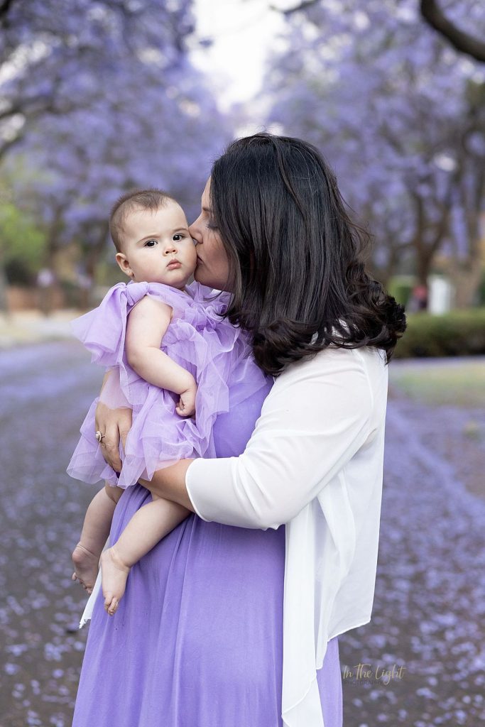 Mom kissing her baby under magical Jacaranda trees in Pretoria.