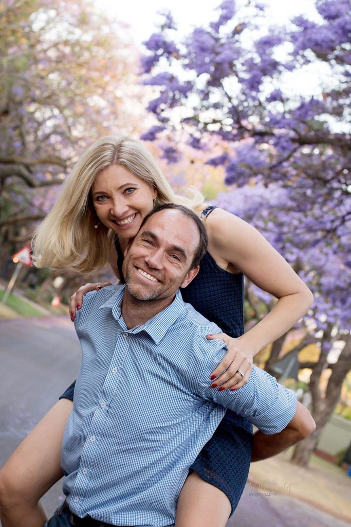 A very happy couple smiling and enjoying life under Pretoria's purple Jacaranda trees.